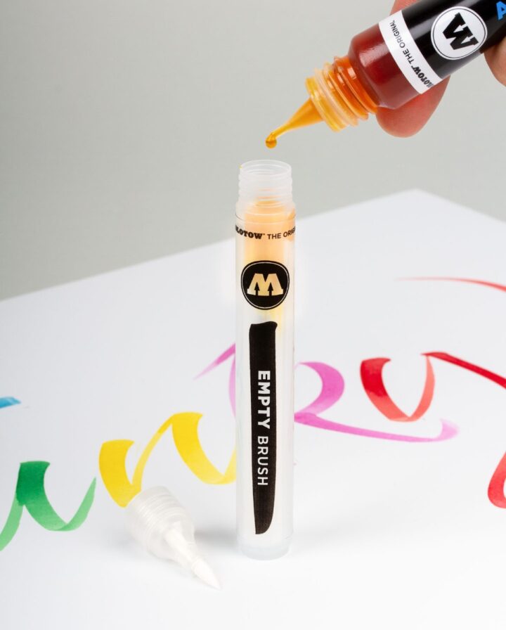 Empty Brush Marker is filled with orange ink and stands in front of colourful lettering