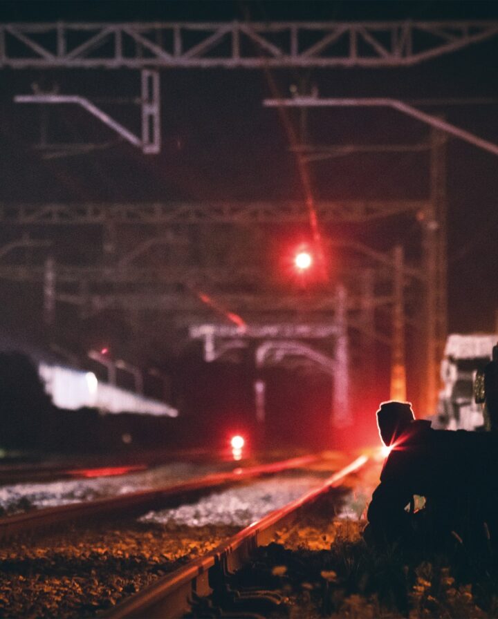 Eine Fotografie von einem Mann, der bei Nacht an rot beleuchteten Bahngleisen sitzt
