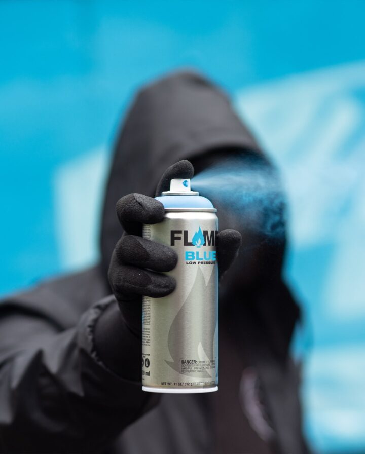Bild von schwarz gekleidetem Mann mit blauer Spraydose in Aktion vor gleichfarbigem Hintergrund