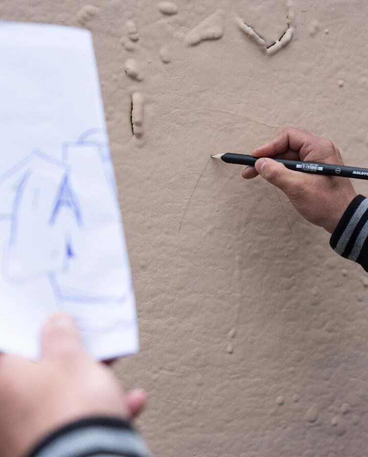 Hand malt mit Maurerbleistift eine Skizze an eine bemalte Mauer