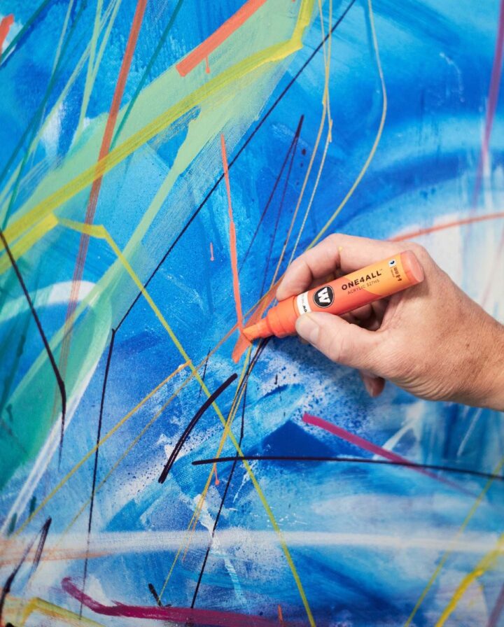 Hand malt mit orangenem Stift auf bunter Leinwand mit blauem Untergrund