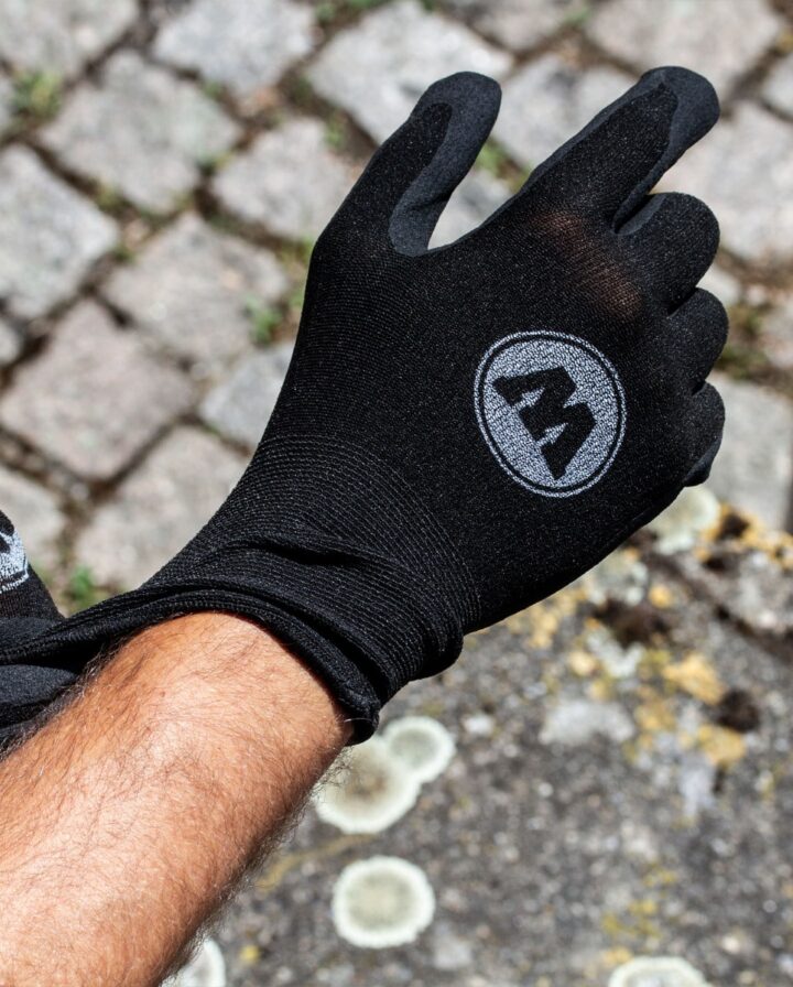 gebräunter Arm zieht einen schwarzen Handschuh mit weißem Logo auf dem Handrücken an
