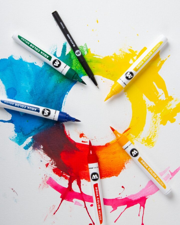 Fünf Exemplare von wasserbasierten Pinselmarkern auf einem damit gemalten Farbkreis mit Aquarelleffekten