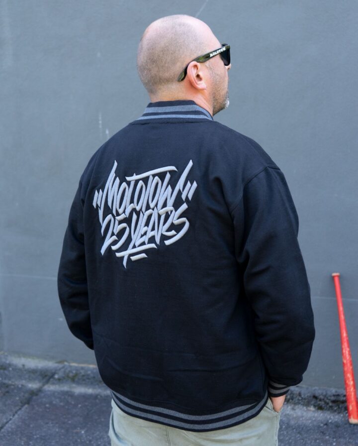 Foto von einem Mann mit einer schwarzen Molotow College Jacke mit grauem Tag als Stickerei auf dem Rücken