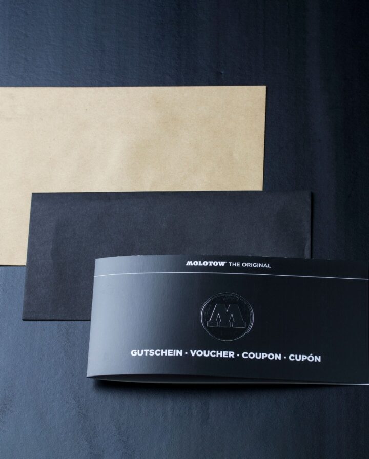 Foto von einem schwarzen Molotow Gutschein der neben einem schwarzen und einem braunen Umschlag liegt